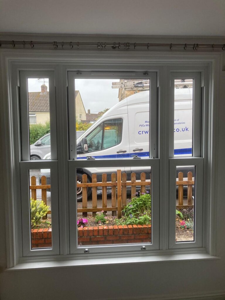 New white UPVC triple-panel casement window viewed from inside, overlooking garden and parked van outside.